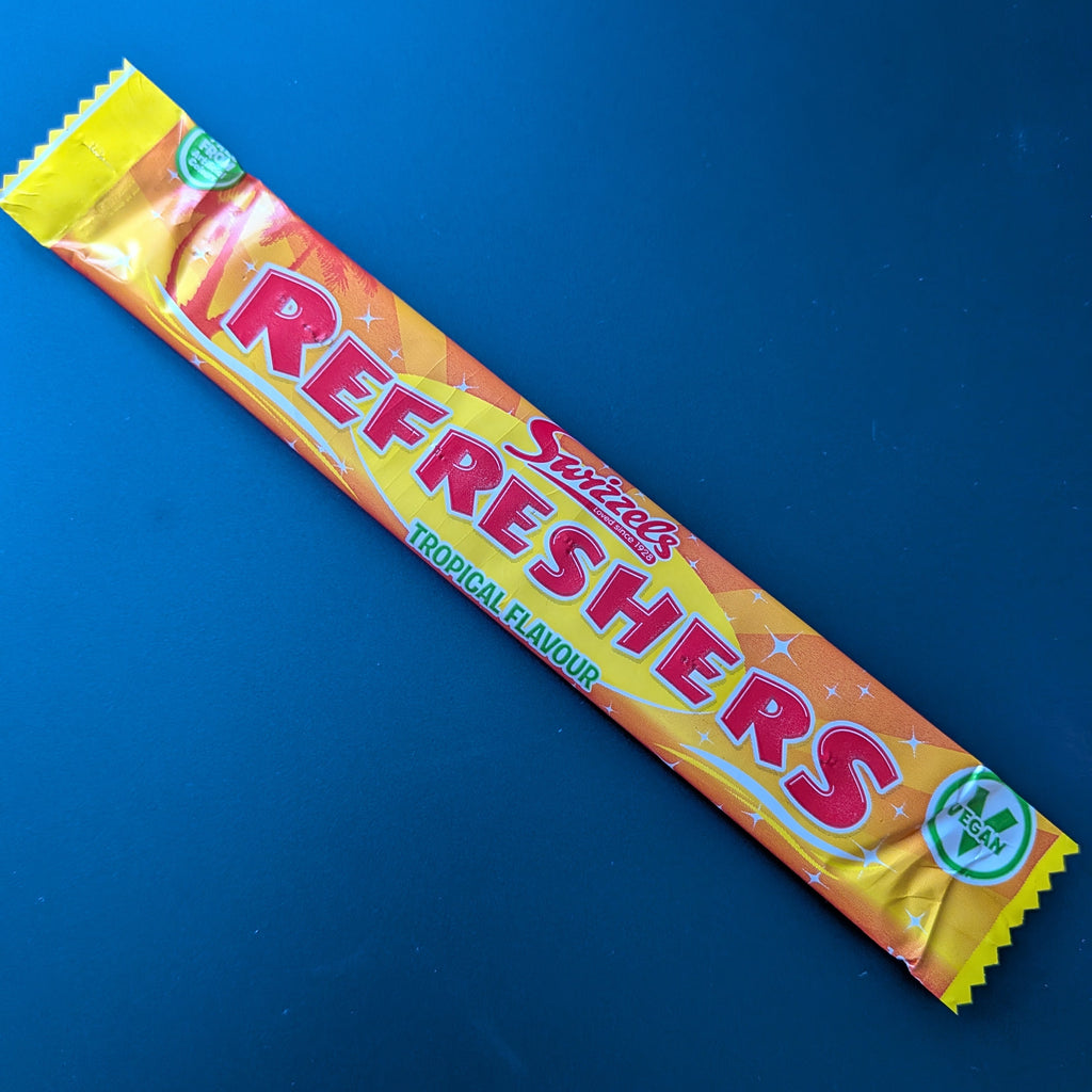 A single wrapped Swizzles Refreshers Tropical Flavour candy bar on a solid dark blue background.