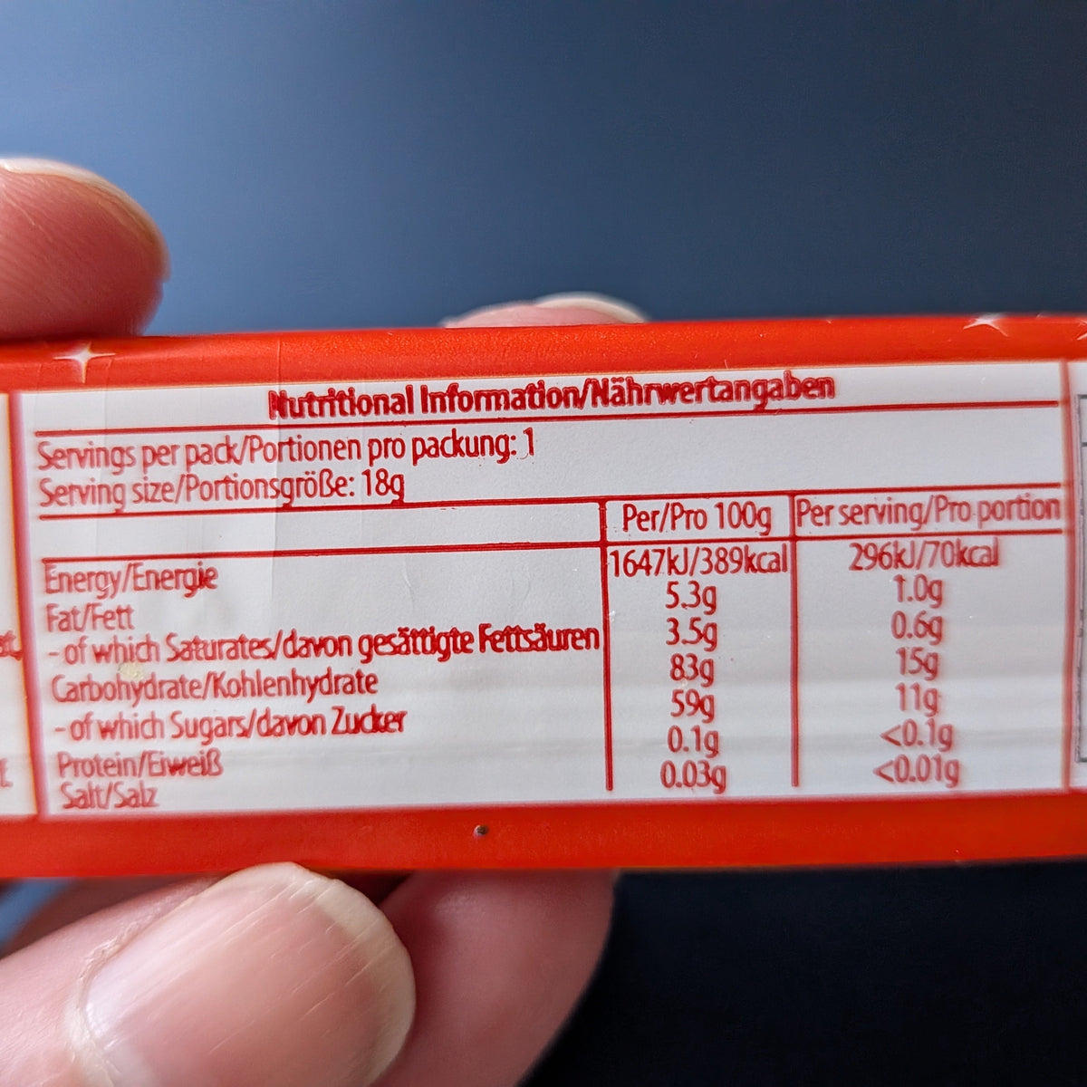 A close-up of a hand holding a package, showing the red and white nutritional information panel with German text and a blue background.